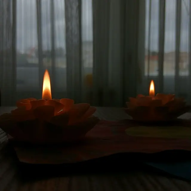 Two lit lotus-shaped candles on a wooden board