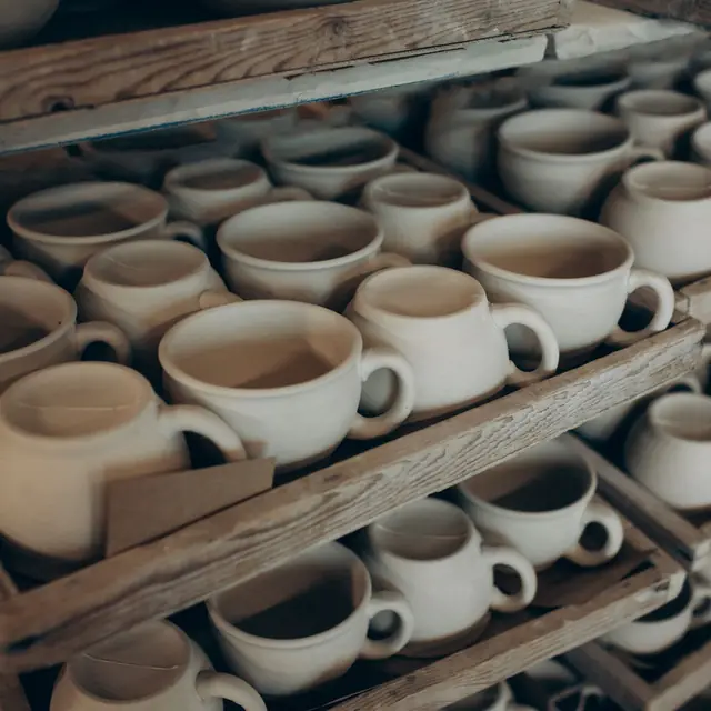 Rows of cream stoneware cups on a wooden drying rack