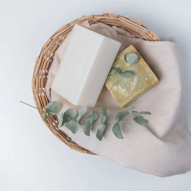 Two soap bars resting in a small woven basket with eucalyptus leaves